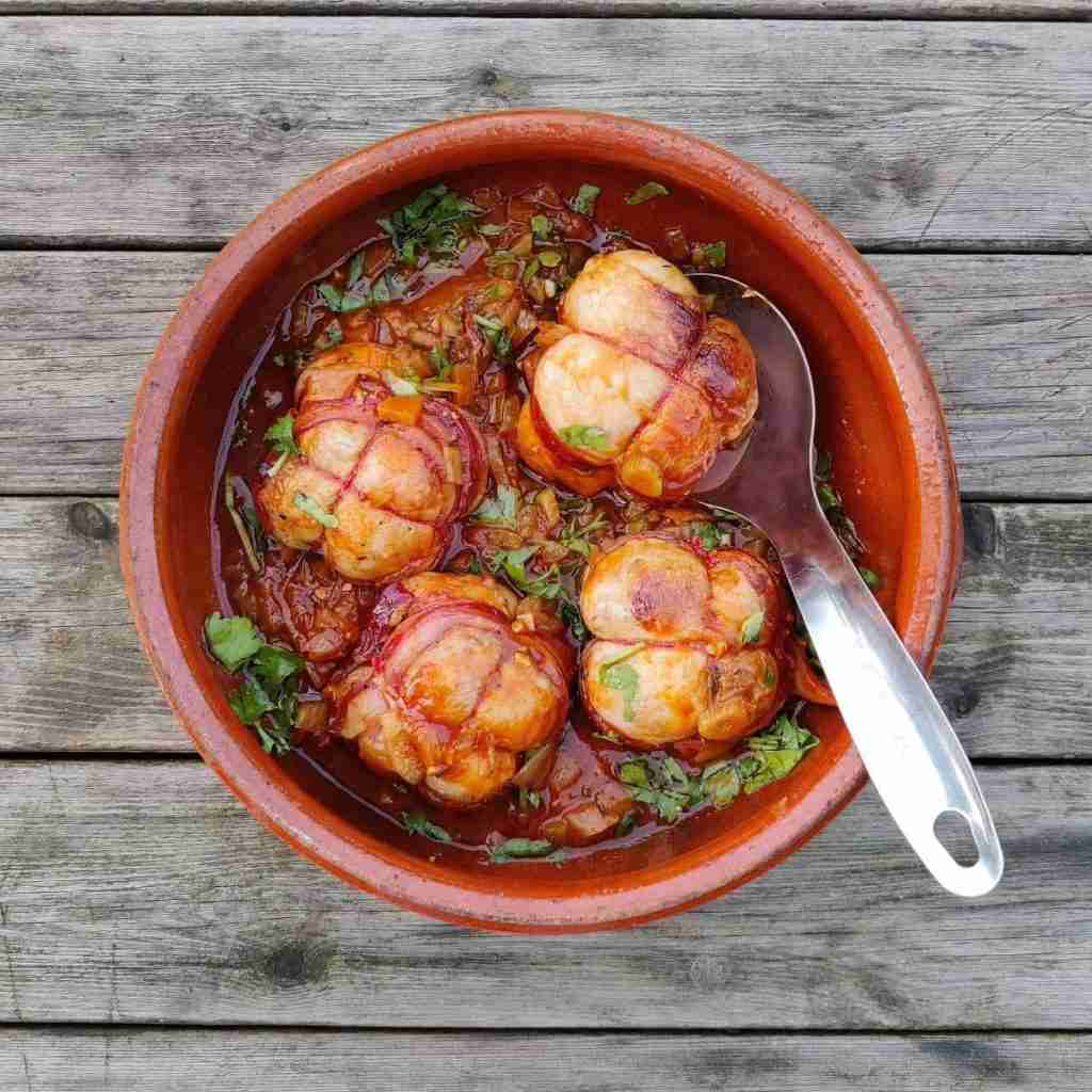 image of a terracotta pot on a wooden table containing four meat parcels in a tomato sauce. You can find the recipe on the blog of cookery school Gourmandises Academie in Cottenham, Cambridge
