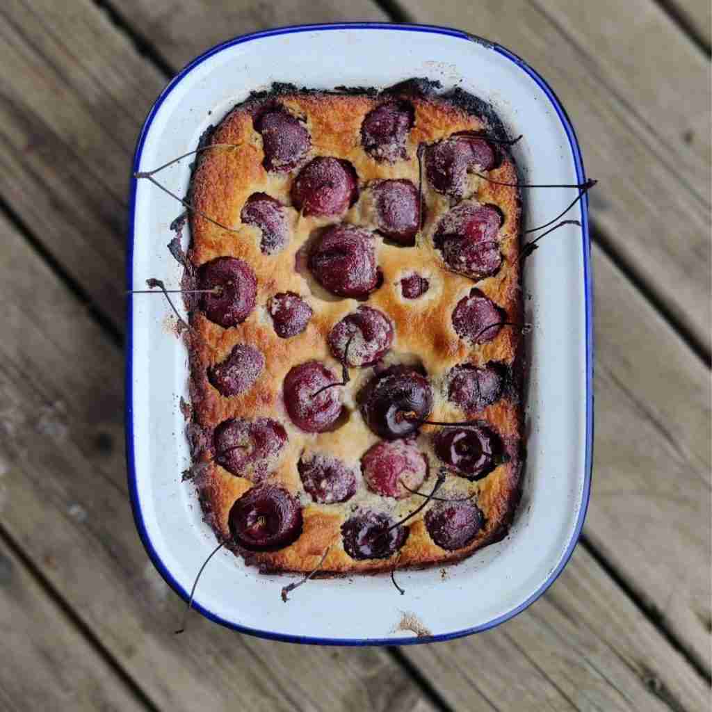 Image with an enamel tin filled with some kind of cherry cake, recipe available on the blog of Gourmandises Academie