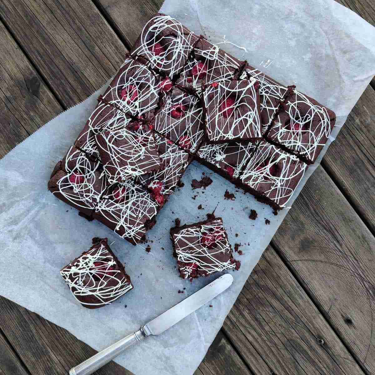 image with pieces of chocolate brownies presented on parchment paper, drizzled with white chocolate, the recipe is available on the blog of cookery school Gourmandises Academie