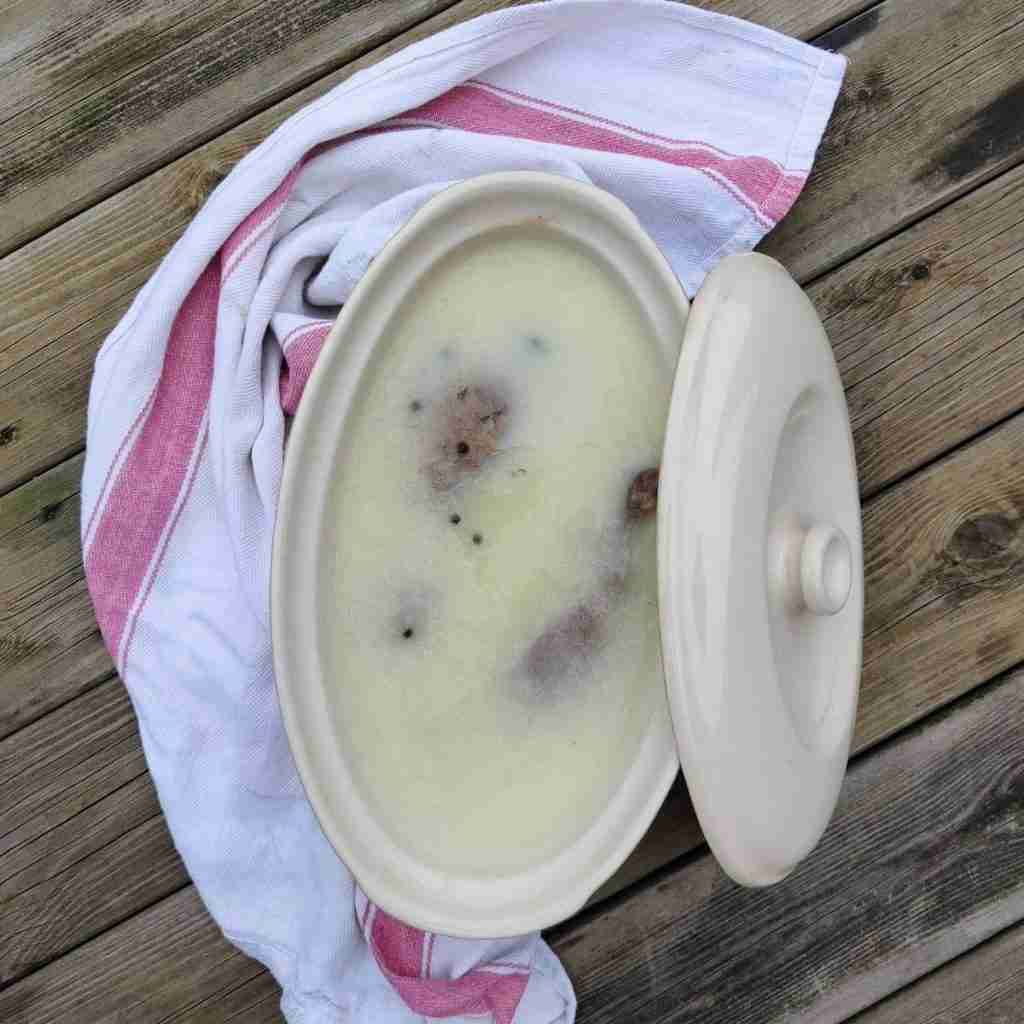 picture of a terrine dish with a cloth around it, filled with goose fat and bits of meat appearing on the surface, you can learn how to make this confit on the blog of cooking school Gourmandises Academie