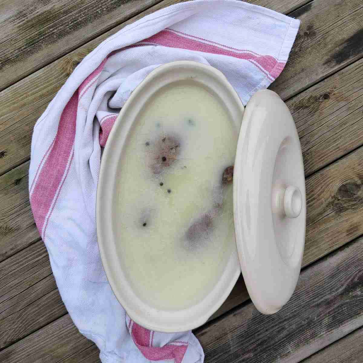 picture of a terrine dish with a cloth around it, filled with goose fat and bits of meat appearing on the surface, you can learn how to make this confit on the blog of cooking school Gourmandises Academie