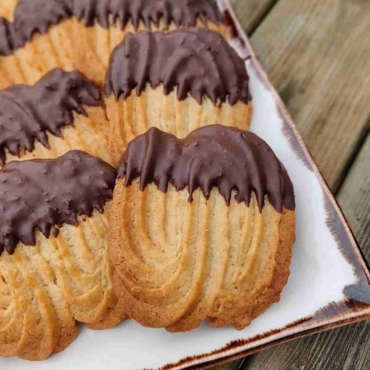 Image of a selection of cookies dipped in dark chocolate, presented on a white tray with brown borders, you can learn how to make these cookies at cookery school Gourmandises Academie in Cambridge