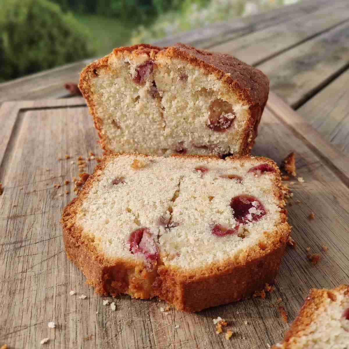 image of a slice of loaf cake with cherries inside, presented on a wooden board, recipe available on the blog of cookery school, Gourmandises Academie, Cambridge