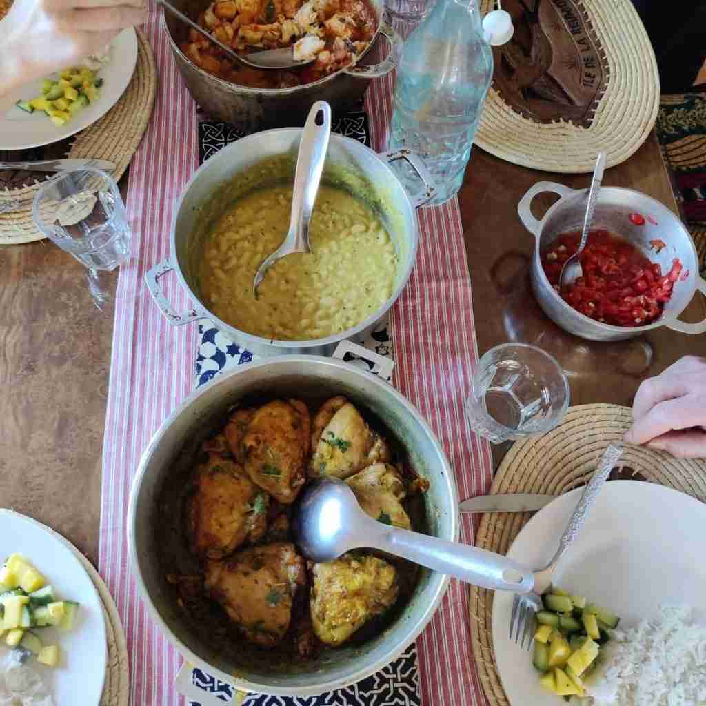 Picture of a table set with three big pans one containing chicken, another beans, and another fish