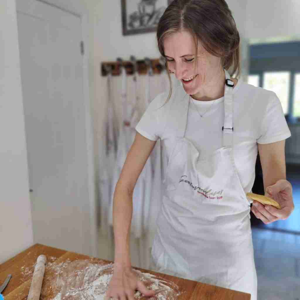 Image of a woman in an apron, a rolling pin, holding pastry on one hand and spreading flour with the other