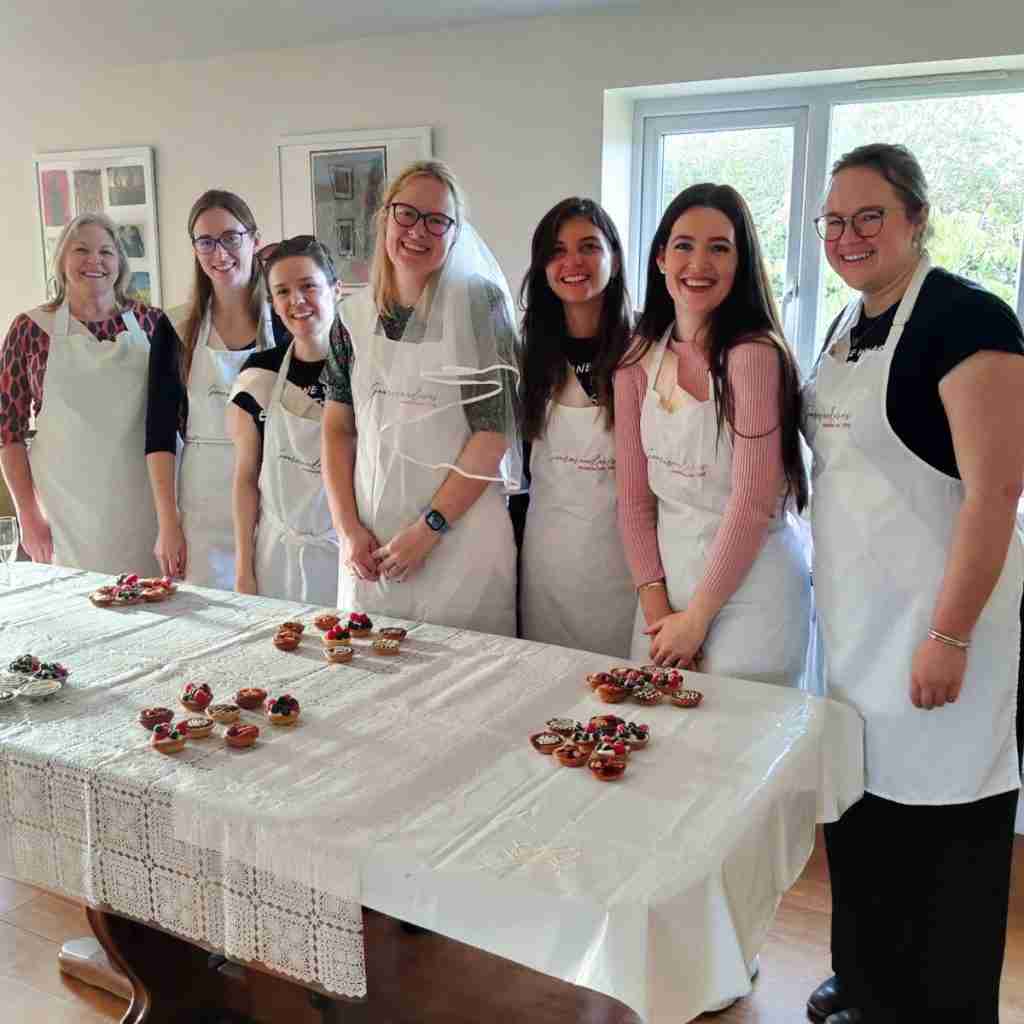 image of 7 girls gathered around a table laden with mini tartellettes after a baking hen party at Gourmandises Academie, Cambridge