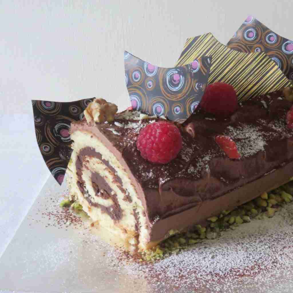 image of a Christmas chocolate roulade, decorated with raspberries and chocolate shards