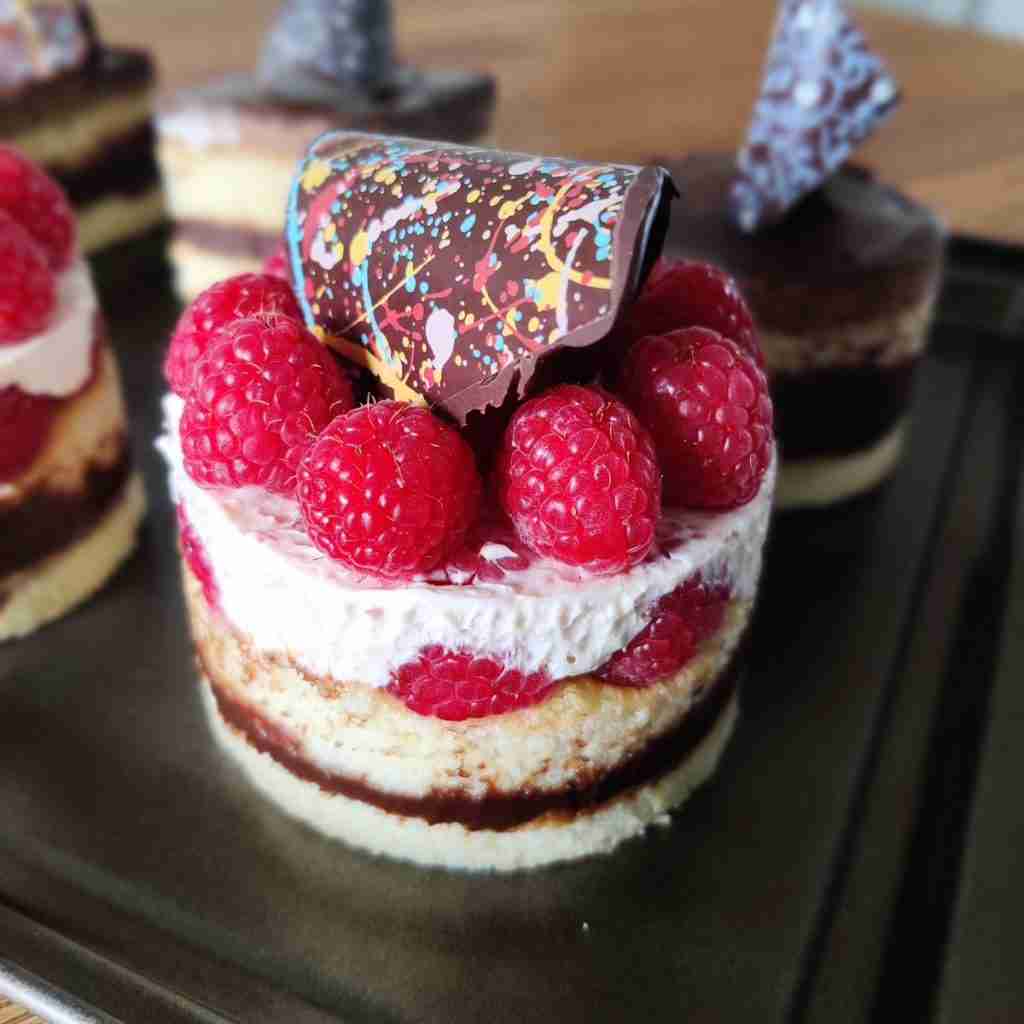 image of a small layered cake with raspberries and a chocolate decoration on top