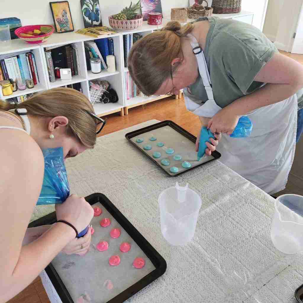 image of two ladies piping pink and green macarons during a macarons class at cookery school Gourmandises Academie, Cambridge