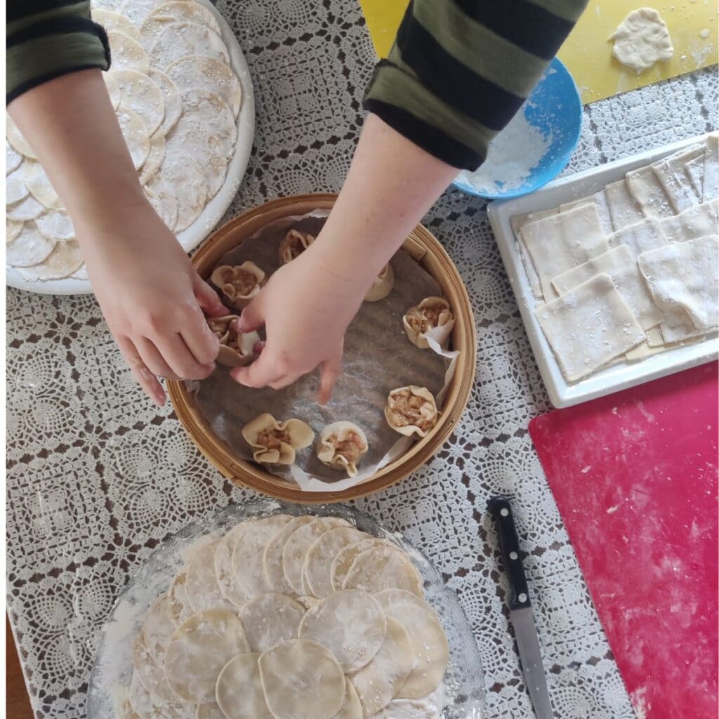 Image of dumpling dough and someone placing the shaped dumplings into the bamboo steamer, photo taken during a dumpling class at cookery school, Gourmandises Academie, Cambridge