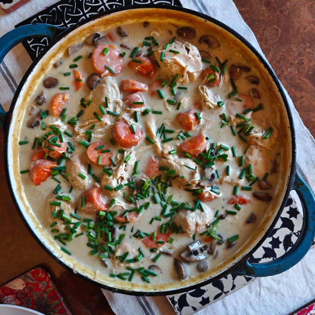 image of a cast iron pan filled with pieces of chicken, carrots and mushrooms, topped with fresh chives in a white sauce, recipe can be found on cookery school Gourmandises Academie, Cambridge