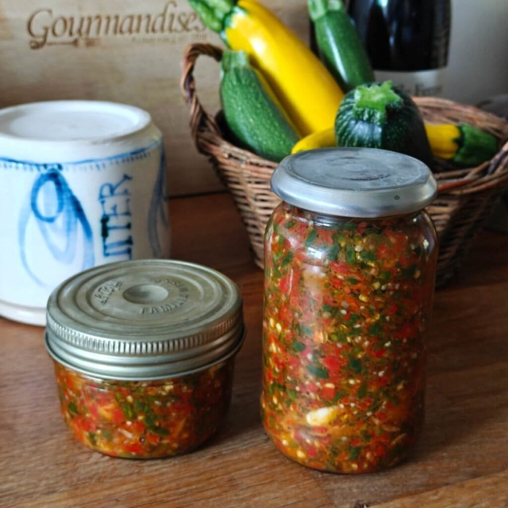 image featuring two jars of chilli paste with a basket of courgettes in the background and a butter bell